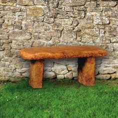 a wooden bench sitting in front of a stone wall with grass growing on the ground