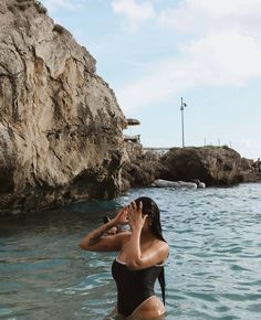 a woman standing in the water talking on her cell phone while wearing a bathing suit