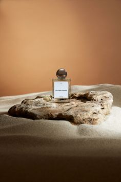 a bottle of perfume sitting on top of a rock in the middle of some sand