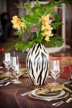 a vase filled with yellow flowers on top of a table next to glasses and plates