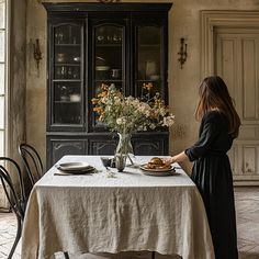 a woman standing in front of a table with food on it and flowers in a vase