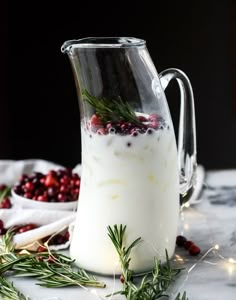 a pitcher filled with white liquid surrounded by cranberries and greenery on a table