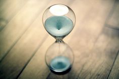 an hourglass sitting on top of a wooden table next to a lit candle in the middle