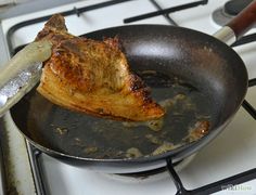 a piece of meat is being cooked in a frying pan on top of the stove