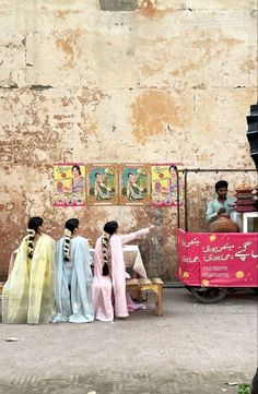 three women in colorful saris sitting on a bench next to a man and woman