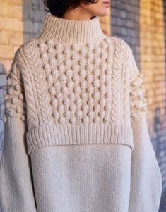 a woman wearing a white sweater and black pants standing in front of a brick wall