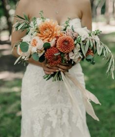 a woman in a wedding dress holding a bouquet of orange and white flowers with greenery