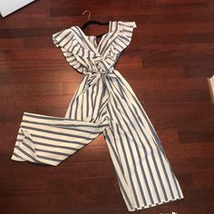 V-Neck Front With Shoulder Ruffles, Tie For The Waist. Striped V-neck Jumpsuits And Rompers For Summer, White Ruffled Jumpsuits And Rompers For Vacation, Casual Ruffled V-neck Jumpsuits And Rompers, Casual Summer Jumpsuits And Rompers With Vertical Stripes, Striped Jumpsuits For Spring Day Out, Casual White Jumpsuits And Rompers With Ruffles, Blue V-neck Jumpsuit With Ruffles, Striped V-neck Jumpsuits For Vacation, Casual Striped V-neck Jumpsuits And Rompers