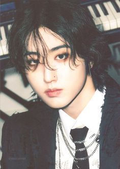 a young man with black hair wearing a suit and tie in front of a piano