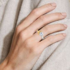 a woman's hand with a diamond ring on her left hand, resting against a white sweater