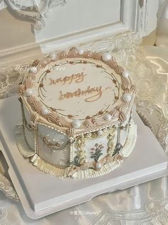 a white and gold decorated birthday cake on top of a silver platter with an ornate design