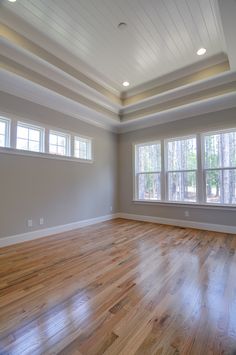 an empty living room with hard wood flooring and white painted walls, two windows on the far wall