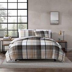 a bed with plaid comforter and pillows in a room next to a large window