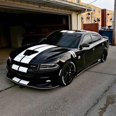 a black and white dodge charger parked in front of a garage with its door open