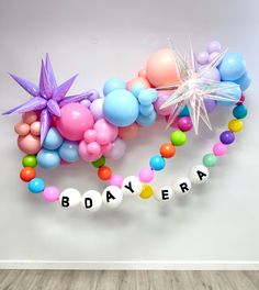 balloons and streamers with the word bdayera spelled out in white letters on a wooden floor