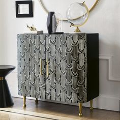 a black and white cabinet with gold handles in a room next to a mirror on the wall