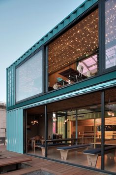 an outdoor dining area with tables and lights on the side of a shipping container building