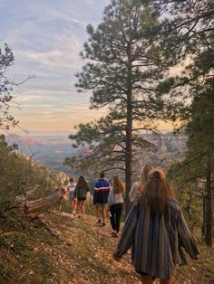 a group of people walking up a hill on a trail in the woods at sunset