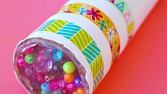 a tube filled with lots of beads on top of a pink surface and colorful paper