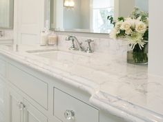 a white bathroom with marble counter tops and double sinks, along with a large mirror on the wall