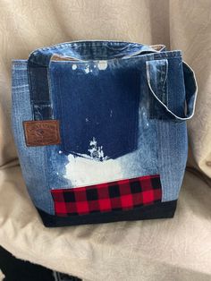 a blue jean purse with red and black patchwork on the front, sitting on a chair