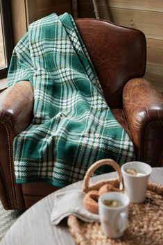 a plaid blanket draped over a chair with two cups of coffee on the table next to it