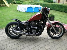 a red and black motorcycle parked on top of a brick road next to a green field