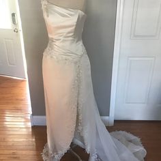 a white wedding dress on display in front of a door with a wooden floor and gray wall