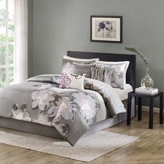 a bed with grey and white comforters in a bedroom next to a window,