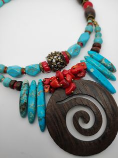 Beautiful ethnic style choker necklace, handmade with various materials: howlite, coral, jasper, hematite, wood. The central element of the necklace is a large pendant made of dark walnut-coloured cut-out wood. The turquoise blue of the jasper and the red of the coral contrast with each other and create a beautiful color combination. The necklace is double stranded, made up of different pearls and shells that create intersections of beautiful shapes and colors. The necklace is rigid but at the same time adheres perfectly to the neck and has an adjustable closure with a 7 cm extension. The necklace is very showy and colourful, in the colors of blue, red and brown, it is reminiscent of summer, the sea...suitable for a low-cut dress for a special occasion. It is a unique design created by me Traditional Turquoise Beaded Necklaces With Wooden Beads, Traditional Turquoise Beaded Necklace With Wooden Beads, Traditional Turquoise Necklace With Wooden Beads, Turquoise Wooden Beads Necklace For Festivals, Adjustable Bohemian Red Coral Necklace, Bohemian Turquoise Necklace With Wooden Beads, Spiritual Turquoise Necklaces With Wooden Beads, Spiritual Turquoise Necklace With Wooden Beads, Artisan Turquoise Necklace With Wooden Beads