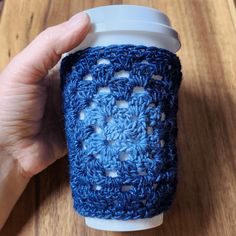 a hand holding a coffee cup cozying it's sleeve with crochet