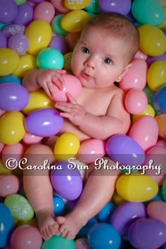 a baby laying in a pile of balloons with his hands on his chest and looking at the camera