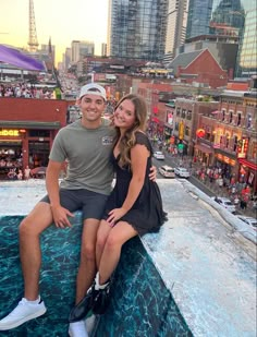 a man and woman sitting on the edge of a building in front of a cityscape