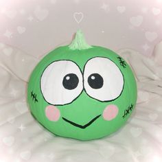 a green pumpkin with eyes and nose painted on it's face, sitting on a bed