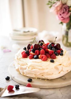 a cake with white frosting and berries on top sitting on a table next to flowers