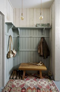 a wooden bench sitting under two hanging lights next to a wall with coat hooks on it