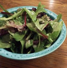 a blue bowl filled with salad on top of a wooden table