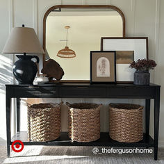 a console table with three baskets under a large mirror and framed pictures on the wall