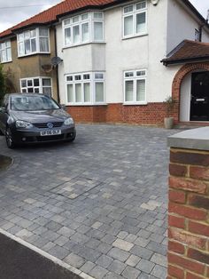 a black car parked in front of a white house on a brick driveway next to a red brick wall