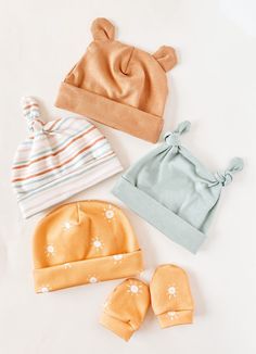 four baby hats and mittens laid out on a white surface