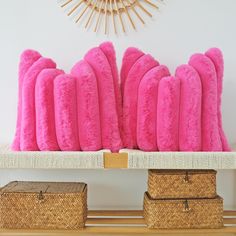 four pink pillows sitting on top of a shelf next to two wicker bins