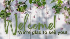 a welcome sign is hanging on the side of a white fence with pink and green flowers