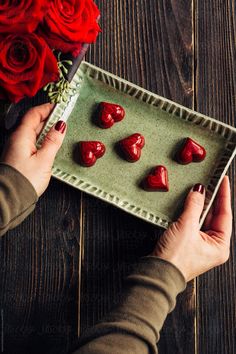 a person holding a tray with chocolates on it next to flowers and red roses