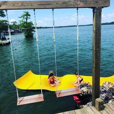 two people sitting on swings in the middle of a body of water near a dock