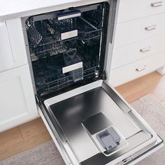 an open dishwasher in a kitchen with white cupboards and drawers on the floor