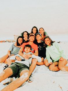 a group of young people sitting on top of a sandy beach next to the ocean