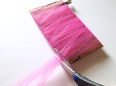 a pair of scissors cutting pink tulle on top of a piece of fabric with the end cut off