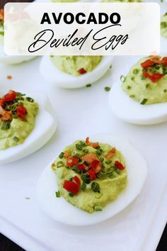 deviled eggs topped with guacamole, tomatoes and green onions on a white platter