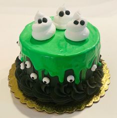 there is a green cake with white frosting and black decorations on the top that looks like eyes