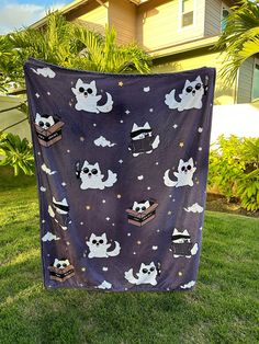 a purple blanket with cats and clouds on it sitting in the grass near a house